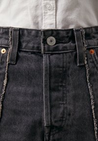 High-waisted black denim jeans with frayed hems, silver hardware, and contrasting orange stitching on the front pockets and waistband.