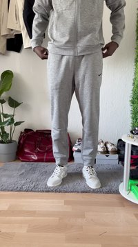 Gray zip-up hoodie with matching sweatpants made of a soft fabric, featuring ribbed cuffs and a small logo on the hoodie. White sneakers.