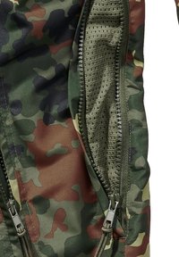 Camouflage-patterned jacket with a partially unzipped pocket showing green breathable mesh fabric inside.