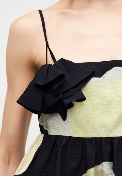 Μαύρο φόρεμα με λεπτομέρεια με βολάν στον ώμο, με εφαρμοστό μπούστο και φούστα με πιέτες. Το ύφασμα έχει απαλό υφή με ελαφρύ μοτίβο.