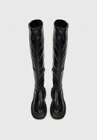 Čierne čižmy po kolená s hladkým koženým povrchom, so zipsom na boku a textúrovanou podrážkou. Vysoký, štruktúrovaný tvar s minimálnymi akcentmi.