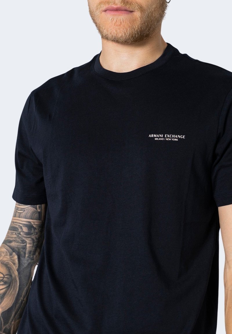 Czarna bawełniana koszulka z okrągłym dekoltem i krótkimi rękawami. Ozdobiona białym logo "Armani Exchange Milano/New York".