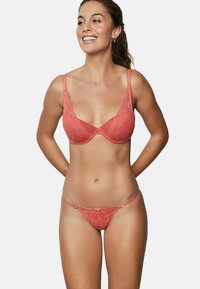 Ensemble de soutien-gorge en dentelle corail et de string, featuring des bretelles délicates, des motifs floraux, des accents en métal doré et un petit nœud sur le string.