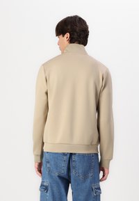 Beige Zip-Up-Sweatshirt mit hohem Kragen, gerippten Bündchen und Saum, kombiniert mit blauen Cargo-Jeans mit mehreren Taschen und einer lockeren Passform.