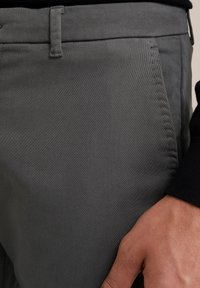 Pantalonii gri conici au un material neted, o ușoară strălucire și cusături precise. Fața este echipată cu bucle pentru centură, îmbunătățind potrivirea și stilul.