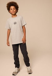 Graues Baumwoll-T-Shirt mit einem runden schwarzen Logo, kombiniert mit schwarzen Cargo-Hosen und hellgrauen Sneakers mit weißen Akzenten.