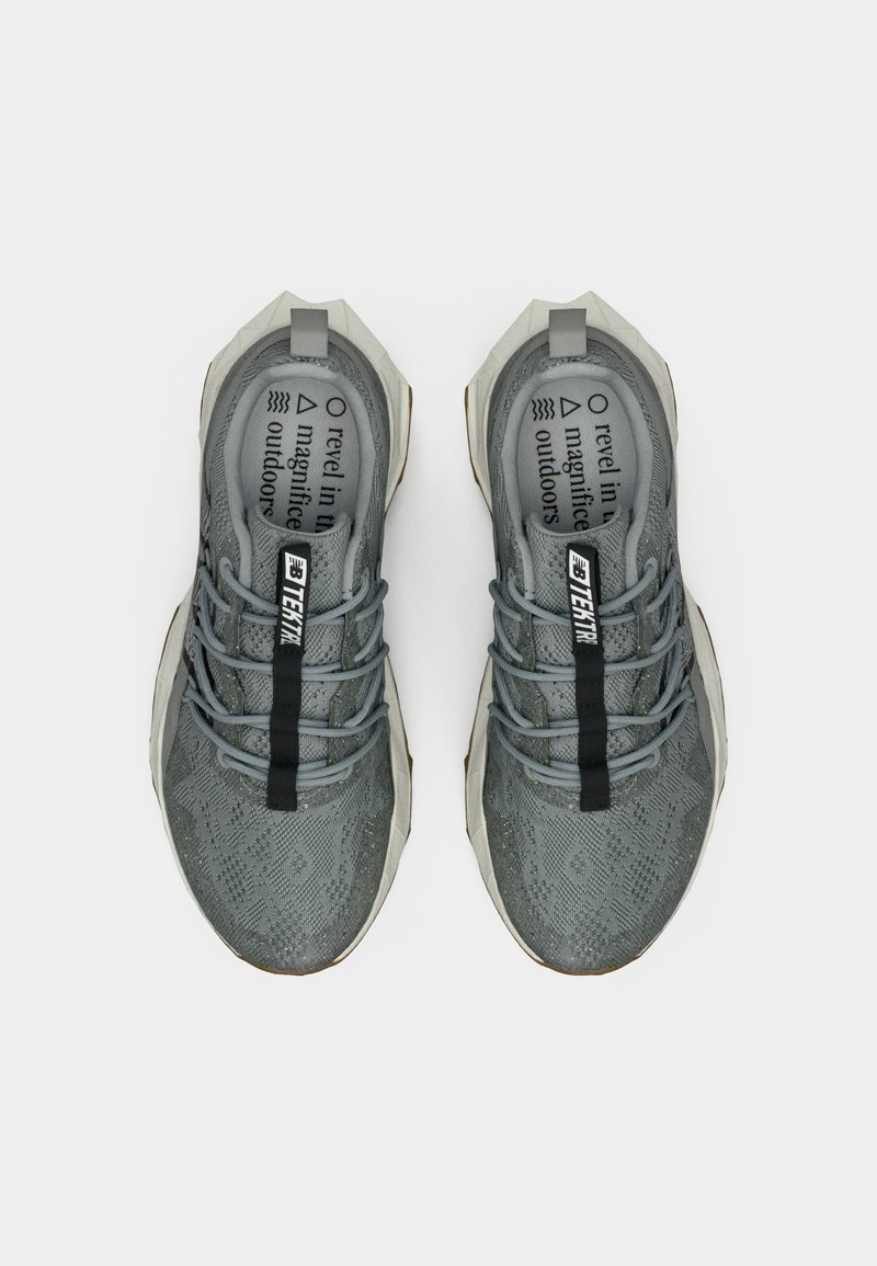 Scarpe da ginnastica grigie con tomaia in rete a motivo, dettagli riflettenti, una fascia nera con il marchio e una suola testurizzata, viste dall'alto.