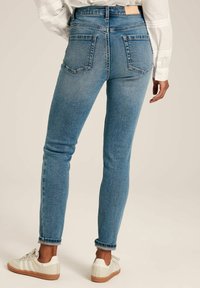 Jeans skinny de denim azul claro con una cintura alta y cinco bolsillos, que presentan un diseño clásico y un ligero desvanecimiento en los muslos y las rodillas.