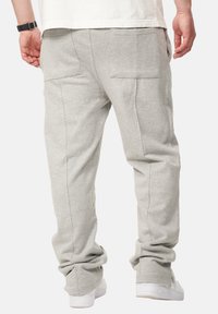 Graue Baumwoll-Sweatpants mit lockerer Passform, ausgestattet mit zwei Gesäßtaschen und gerippten Bündchen an den Knöcheln. Schlichte Stofftextur.