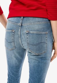 Ljusblå denimjeans med en åtsittande design, som har två bakfickor med böjd sömnadsdetalj och kontrasterande orange tråd.