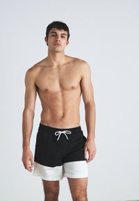 Svarte og hvite badedrakter med elastisk midje og hvit snor. Shortsene har et to-farget design og en avslappet passform.