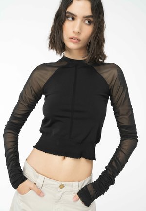 Top nero a maniche lunghe con maniche in rete trasparente, design aderente, texture a coste, lunghezza crop e dettagli di cucitura sottili.