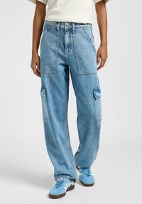I pantaloni cargo in denim blu chiaro presentano una vestibilità oversize, numerose tasche ampie e un design a vita alta. Tessuto testurizzato con dettagli di cucitura visibili.