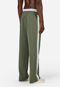 Green relaxed-fit pants with white side stripes, elastic waistband, and soft fabric texture. Features a loose silhouette and full length.