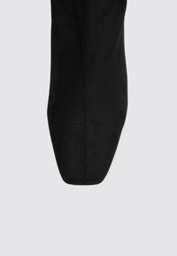 Black suede ankle boot with a pointed toe, visible seam detail, and smooth texture, set against a neutral background.