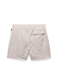 Lichtbeige shorts met een gestructureerd patroon, elastische tailleband en een enkele achterzak met klep. Ruwe oppervlakte details zichtbaar.