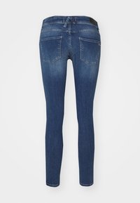 Jeans ajustados en denim azul oscuro, con cinco bolsillos y una cinturilla, textura suave y un ligero desgaste hacia las rodillas.