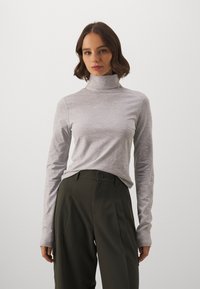 Hele hallimehised turtleneck-särk pikkade varrukatega, valmistatud pehmest kangast. Kombineeritud tumeroheliste kõrge vöökohaga pükstega, millel on külgmised voldid.