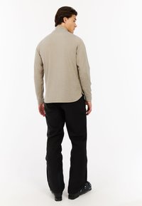 Licht beige langslievend shirt met een textuurafwerking, zijsplitsingen en een mao-kraag, gecombineerd met zwarte skibroeken en laarzen.