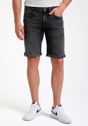 Sorte denimshorts med opsmøget nederkant, der har fem lommer og en frontknaplukning. Båret med hvide sneakers med en sort swoosh-design.