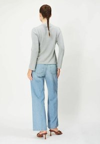 Harmaa pitkähihaisista paita, vaaleansiniset leveälahkeiset farkut, ruskeat korolliset sandaalit, sileä koostumus, ja letitetty poninhäntä näkyy takaa.