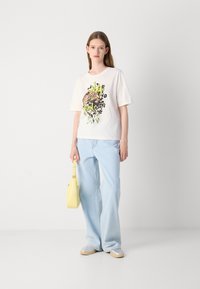 Lysfarget bomulls-T-skjorte med leopardgrafikk, kombinert med løse lyse blå jeans og en gul håndveske. Fritidssko med beige såler.