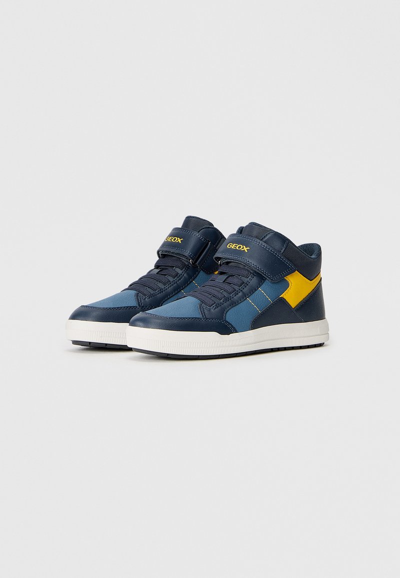 Sneaker alte con una tomaia sintetica blu e blu navy, cinturino in Velcro, suola in gomma bianca e dettagli gialli.