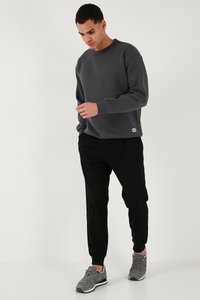 Sudadera gris con cuello redondo, puños acanalados y parche con logo, combinada con pantalones jogger negros y zapatillas deportivas grises. Diseño minimalista.