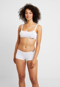 Weißer Baumwoll-Bralette mit verstellbaren Trägern und passenden weißen Boyshorts, die eine glatte Textur und ein dezentes Markenzeichen aufweisen.