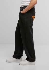 Schwarze weit geschnittene Jeans aus Denim, mit einem bunten bestickten Design auf der Gesäßtasche, mit glatter Textur und geradem Schnitt.