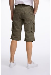 Olivgrüne Cargo-Shorts mit einem elastischen Bund, zwei Seitentaschen und zwei Gesäßtaschen. Getragen mit weißen Turnschuhen.