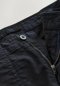 Dark blue pants with a partially open metal zipper and a closed button on the waistband, showing detailed stitching and fabric texture.