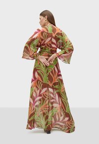 Robe maxi en tissu semi-transparent avec un motif floral dans des tons de rose, vert et marron. Manches longues en forme de cloche et taille ceinturée.