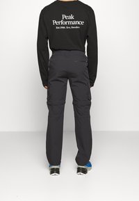 Chemise noire à manches longues avec texte blanc au dos, associée à un pantalon cargo gris foncé doté de poches latérales et d'une coupe décontractée.