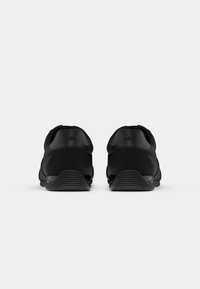Zwarte sneakers met een gladde textuur, lage pasvorm en een subtiel logo op de hiel. Voorzien van een gekartelde zool voor grip.
