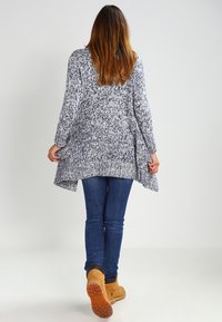 Texturerad, långärmad, öppen cardigan i marinblå och vita mönster, tillsammans med blå jeans och bruna arbetsstövlar.