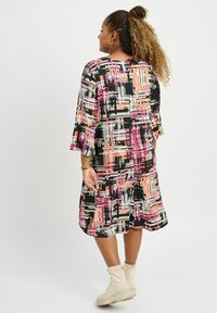 Vestido estampado con mangas acampanadas, fondo negro, líneas geométricas en rosa y beige, hasta la rodilla, hecho de una tela ligera.