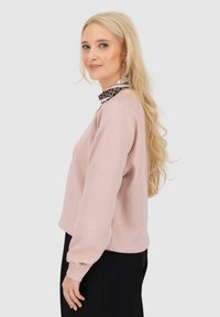 Roze sweatshirt met lange mouwen en een relaxte pasvorm. Heeft een patroon op de kraag. De stof lijkt zacht met een gladde textuur.