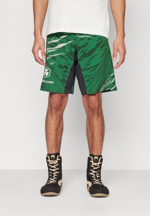 Green patterned shorts featuring black side panels, made of lightweight material, paired with black high-top shoes with gold accents.