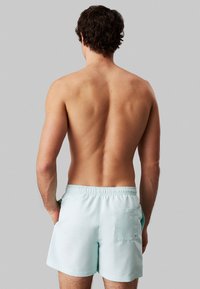 Pantaloni da bagno azzurri chiari realizzati in tessuto resistente, con vita elasticizzata e una tasca sul retro. Texture liscia e leggera.