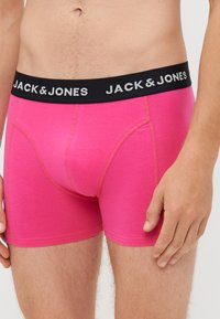 Roza bokserice iz mehkega blaga, z črnim pasom, na katerem je v srebrni barvi natisnjeno "JACK & JONES". Tesno prileganje, gladka tekstura.
