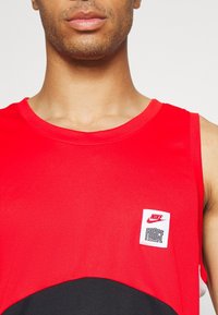 Débardeur de sport rouge en tissu respirant, avec des accents noirs et une étiquette Nike blanche portant le texte « FORCE » à l'avant.