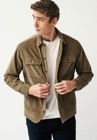 Brown corduroy jacket with two chest pockets, double-button closure, and a lightweight lining, worn over a white t-shirt.