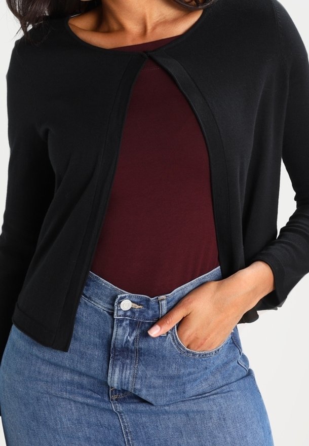 Cárdigan negro con escote redondo, abertura frontal y mangas largas, superpuesto sobre una blusa color burdeos y jeans de tiro alto azules. Textura suave.