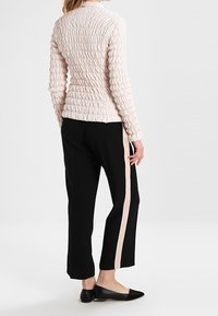 Giacca rosa chiaro texturizzata con tessuto arricciato, abbinata a pantaloni neri con una striscia rosa laterale e scarpe nere basse.