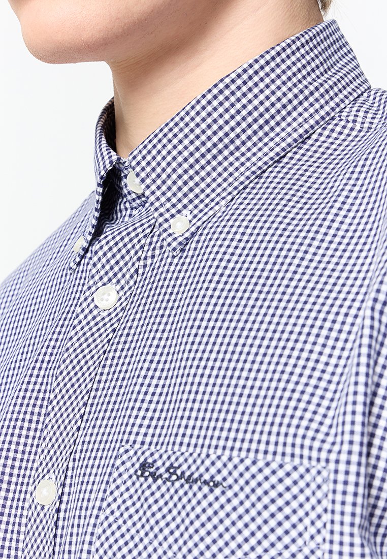 Camisa de cuadros en azul y blanco con cuello abotonado, botones blancos y un bolsillo en el pecho que presenta un branding bordado sutil.