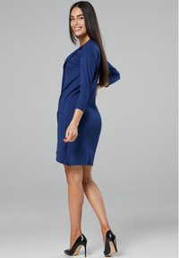 Navy blue knee-length dress with three-quarter sleeves, tailored fit, smooth texture, and paired with black high-heeled shoes.