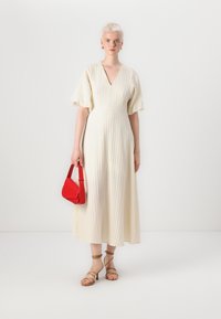 Krämfärgad knälång klänning med V-ringning och puffärmar. Matchad med en röd handväska och beige remsandaler. Texturerat tyg.