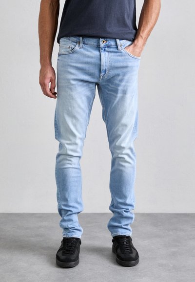Jasnoniebieskie dżinsy o slim fit, z wyblakłą fakturą, pięcioma kieszeniami i subtelnymi detalami stębnowania, w połączeniu z czarnymi sneakersami.
