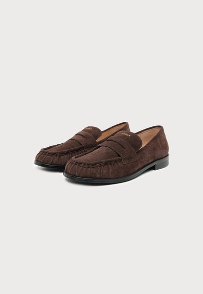 Двойка кафяви велурени лофери с черни подметки и шити детайли, поставени на прост светлосив фон.